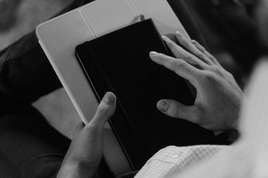 Black and white image of hands holding a book and tablet, representing focused, thoughtful and evidence-based counselling approach