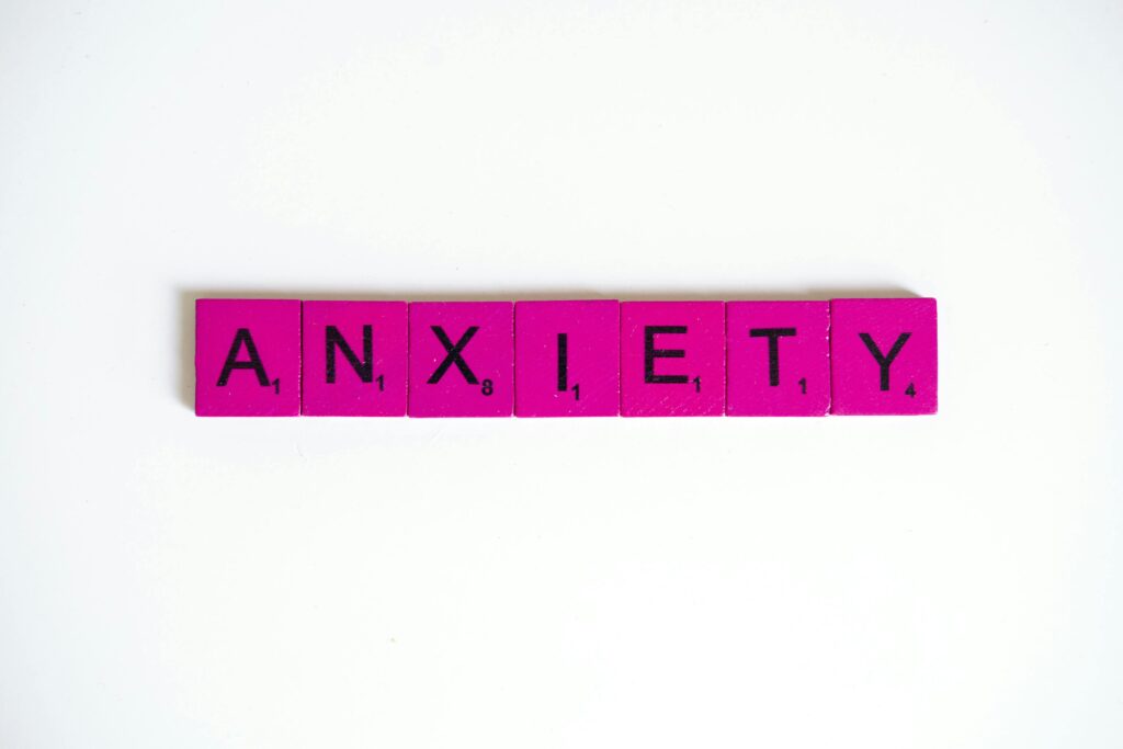 The word anxiety spelled out in pink Scrabble tiles on a neutral background