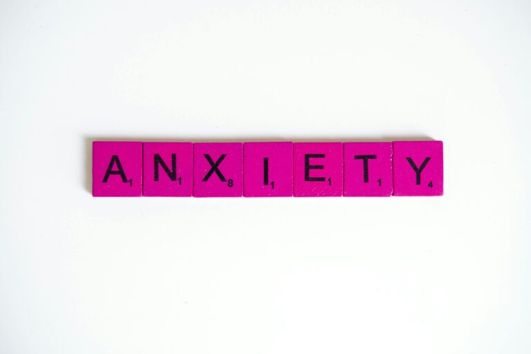 Pink Scrabble tiles spelling 'anxiety' on a white surface. Concept of mental health.