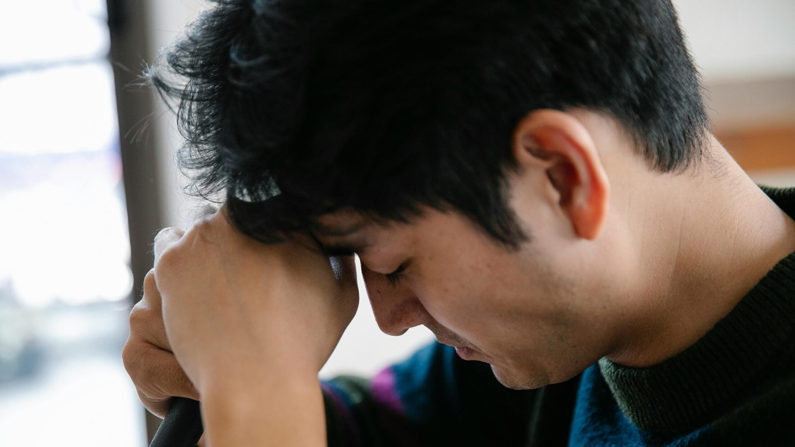 Asian man sitting with head in hands, expressing emotional distress and the weight of unresolved trauma