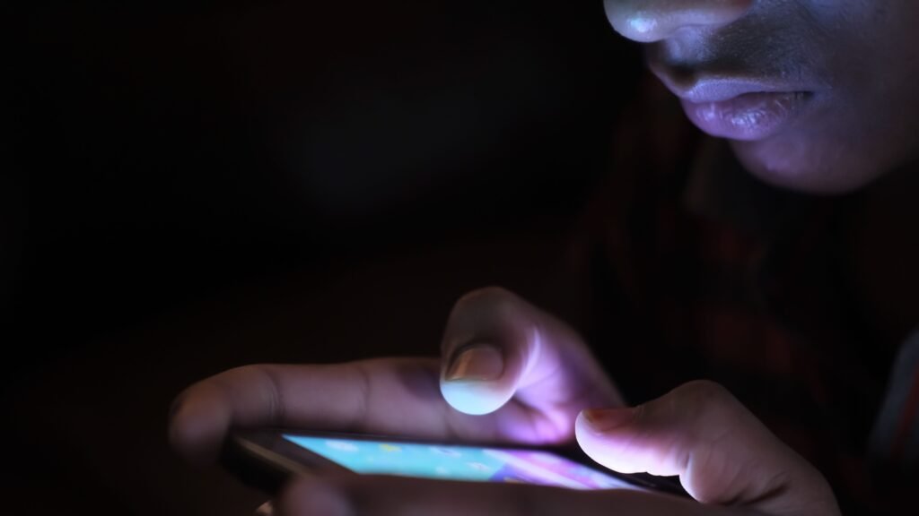 A man using phone to watch porn A man lying in bed at night, illuminated by the glow of his mobile phone screen, scrolling in the dark — illustrating compulsive porn use and the hidden struggle many men face alone.