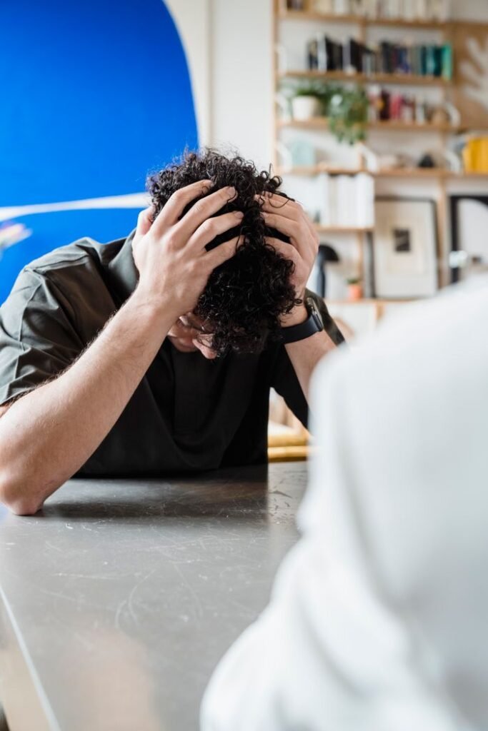 A young man experiencing emotional distress during a counseling session, indoors.
